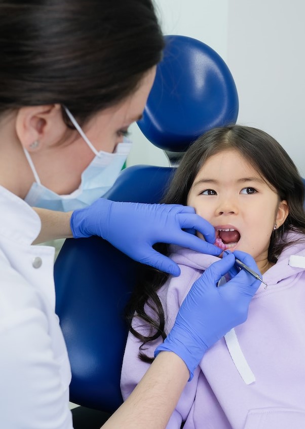 Woman in White Button Up Shirt Wearing Face Mask Cleaning the Girl's Teeth